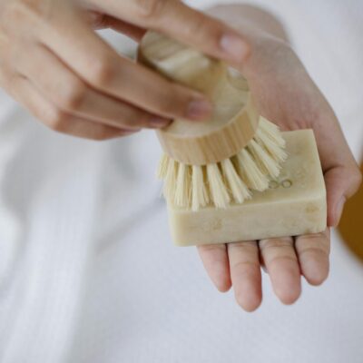 Crop unrecognizable female with eco friendly brush and soap block preparing for skin care on blurred background