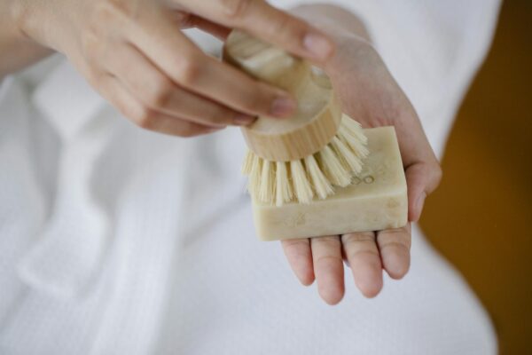 Crop unrecognizable female with eco friendly brush and soap block preparing for skin care on blurred background